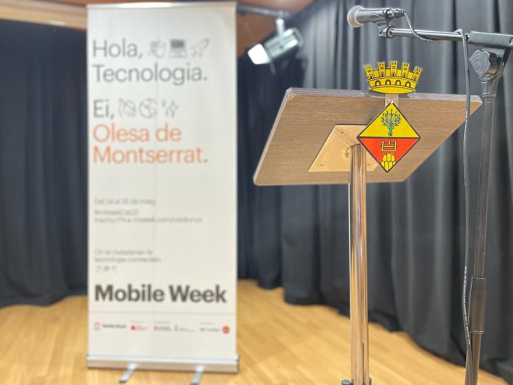 Cartell Hola tecnologia del Mobile Week en segon pla i en primer pla el faristol amb el logo de l'ajuntament